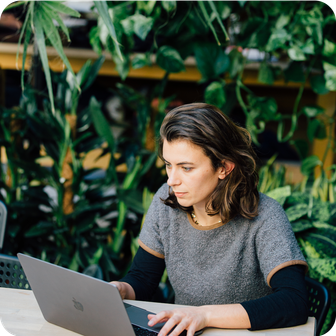 Woman on laptop with green foliage in background