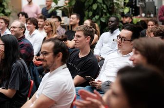 Audience attentively listening to a speaker during a conference, seated in rows.