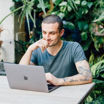 Man in blue t-shirt with tattoos looking at laptop